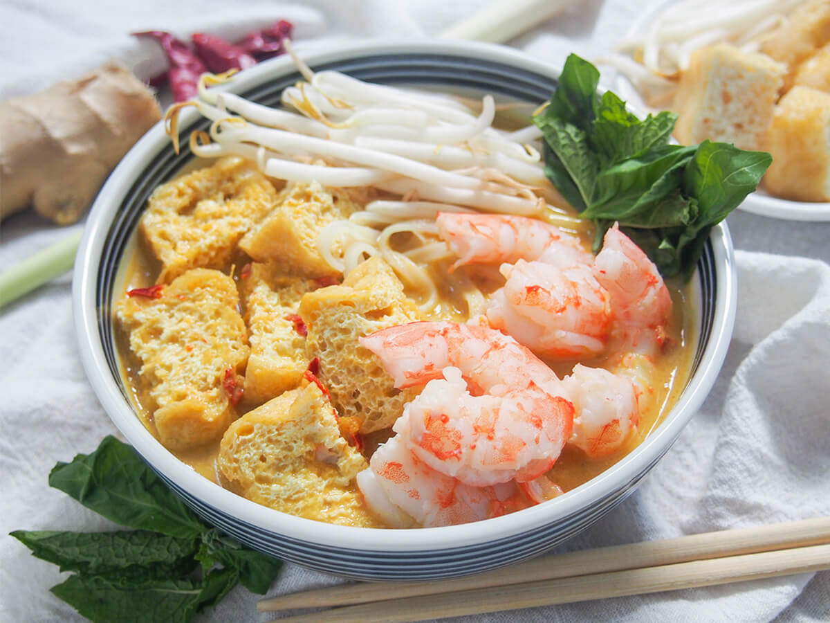 bowl of Singapore laksa bowl of Singapore laksa with herbs and extra toppings behind.