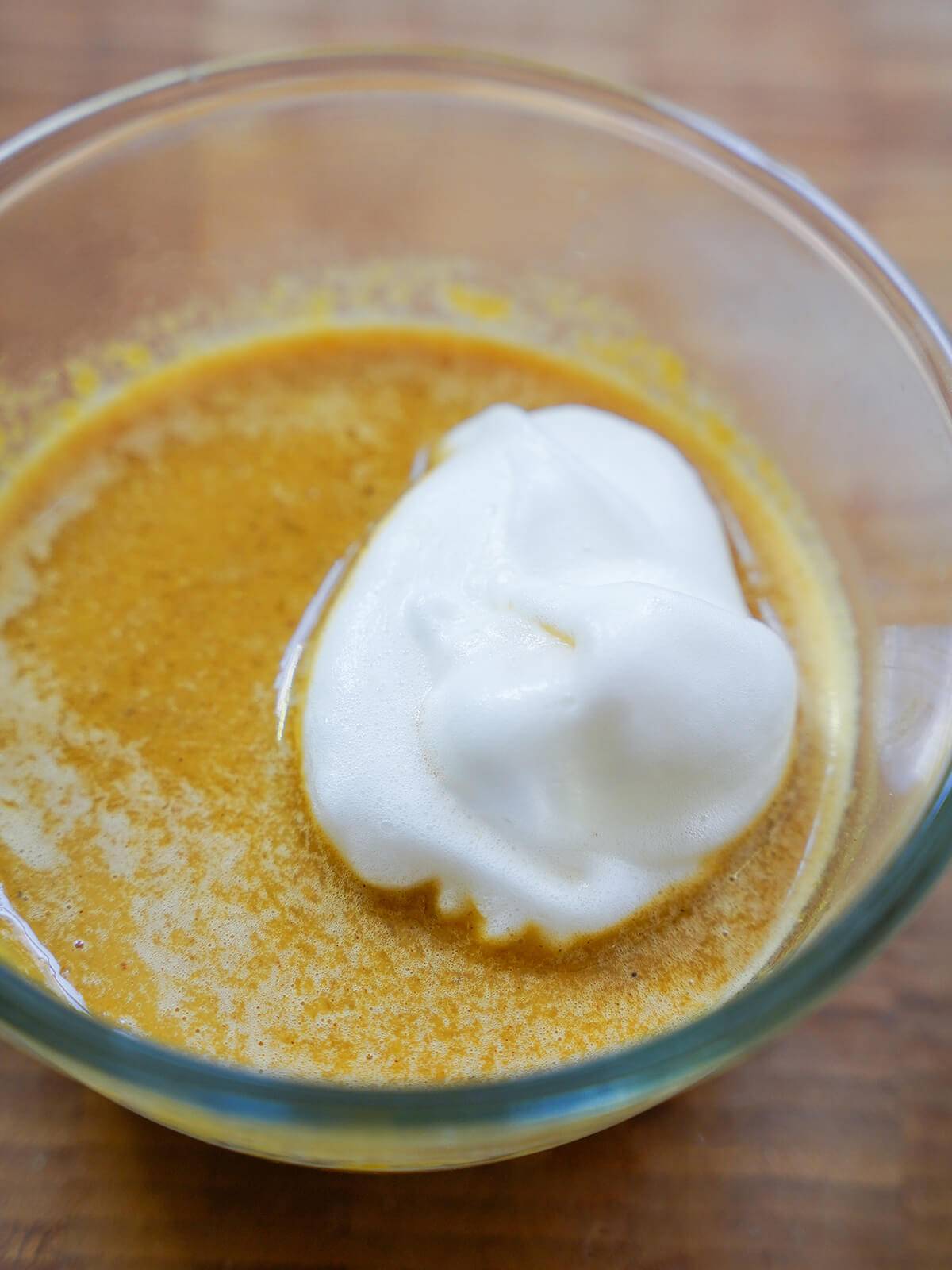 mixing pumpkin souffle a scoop of egg white/meringue on top of pumpkin custard base in a bowl.