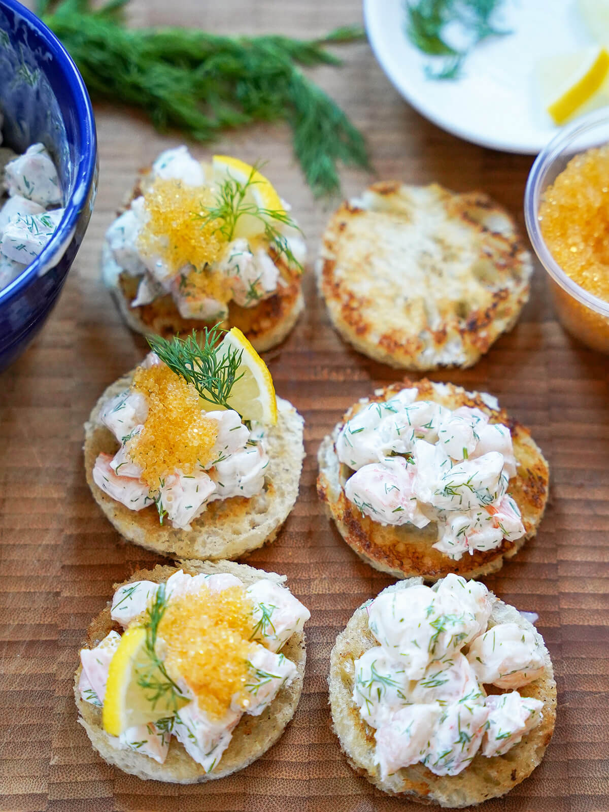 adding shrimp salad and other toppings to pieces of toasted bread.