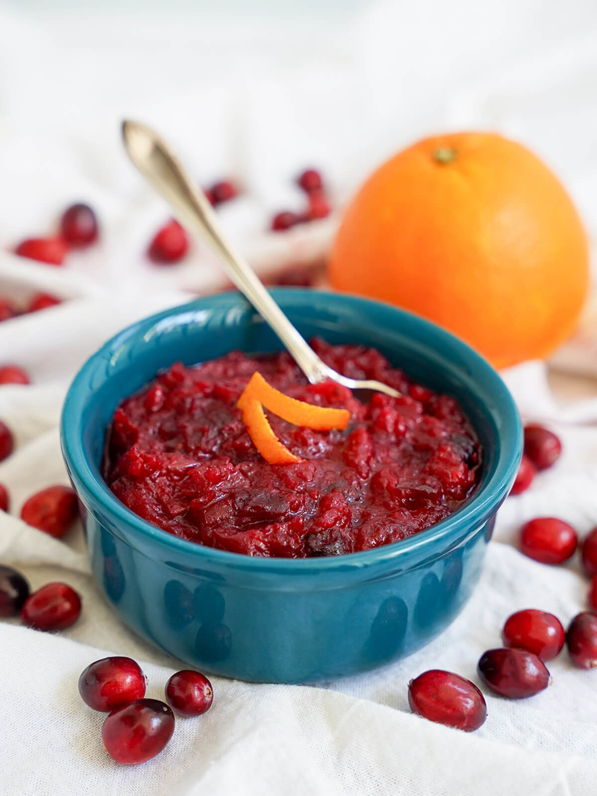 dish of cranberry sauce with orange behind and cranberries around the dish.
