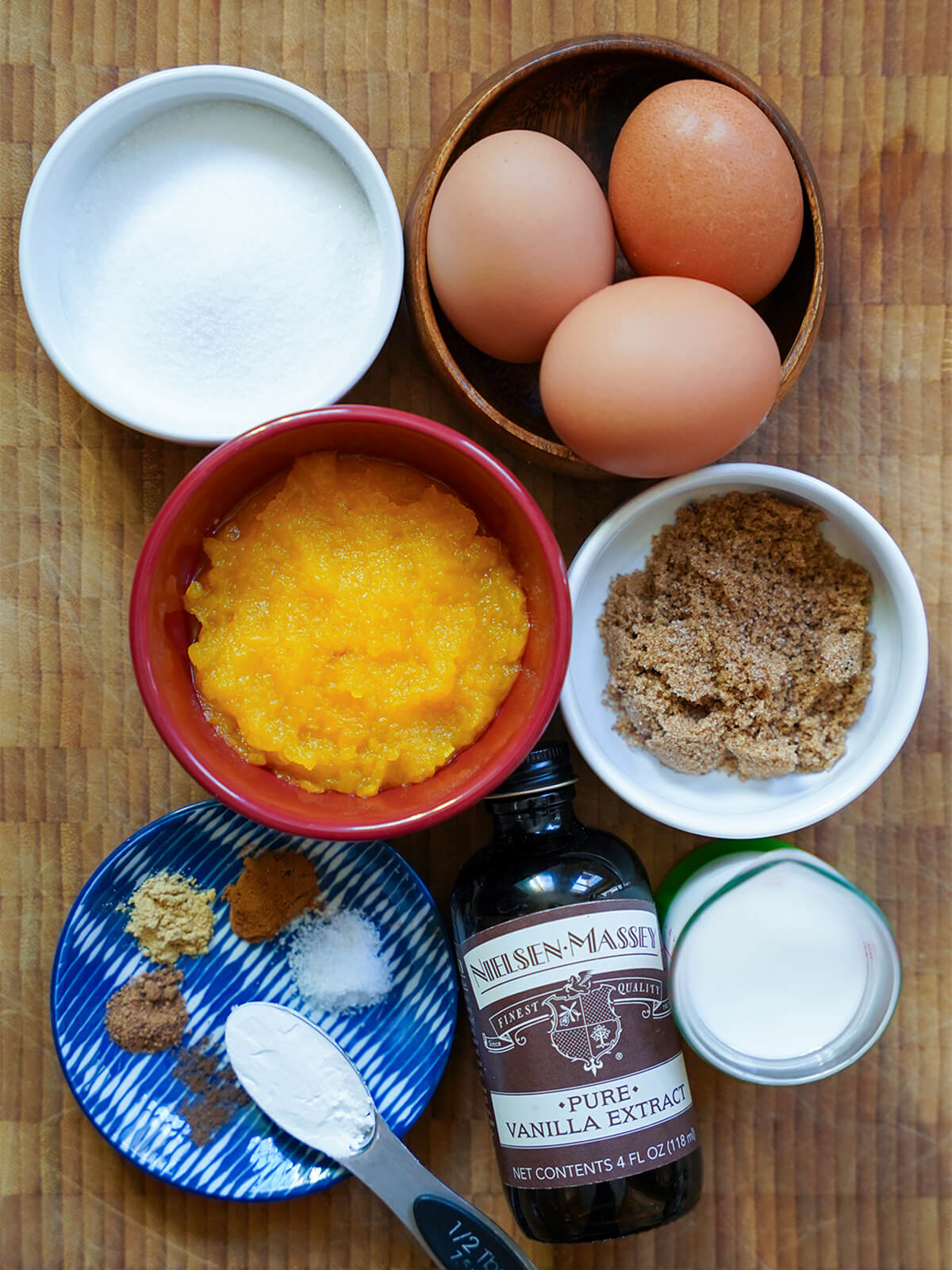 ingredients for pumpkin souffle bowls of eggs, sugar, pumpkin puree with a small plate with spices and measure of milk below.