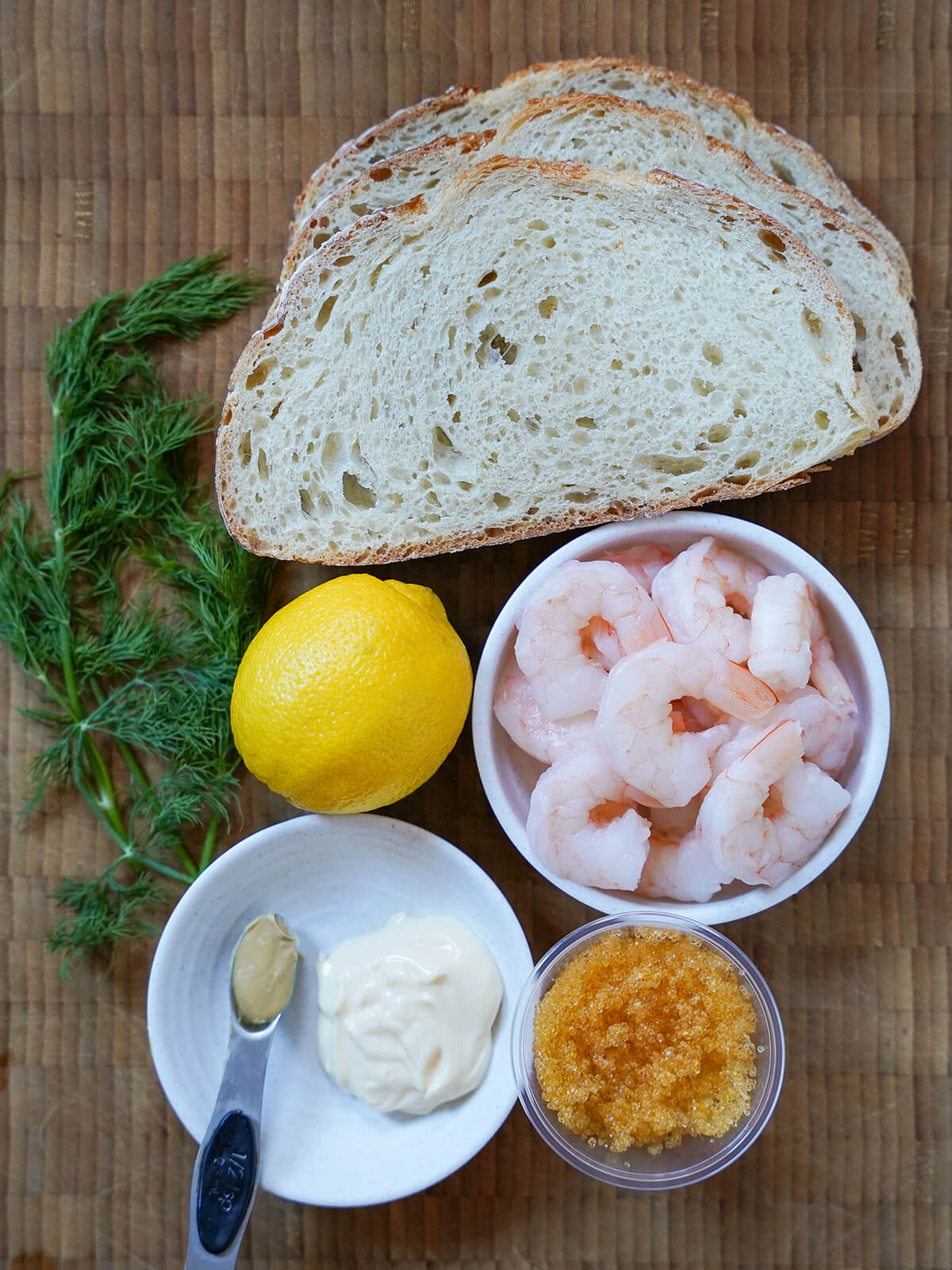 pieces of bread, dishes with shrimp, fish roe and mayonnaise with lemon and dill to side.
