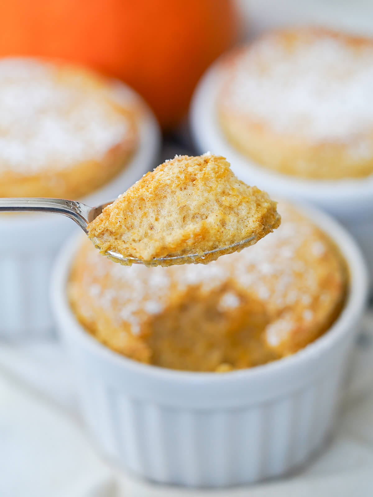 Whether you're looking for a tasty fall-flavored dessert or a gluten free take on pumpkin pie, this pumpkin souffle is a great choice. Gently spiced, light and delicious. a spoonful of pumpkin souffle held over dish.