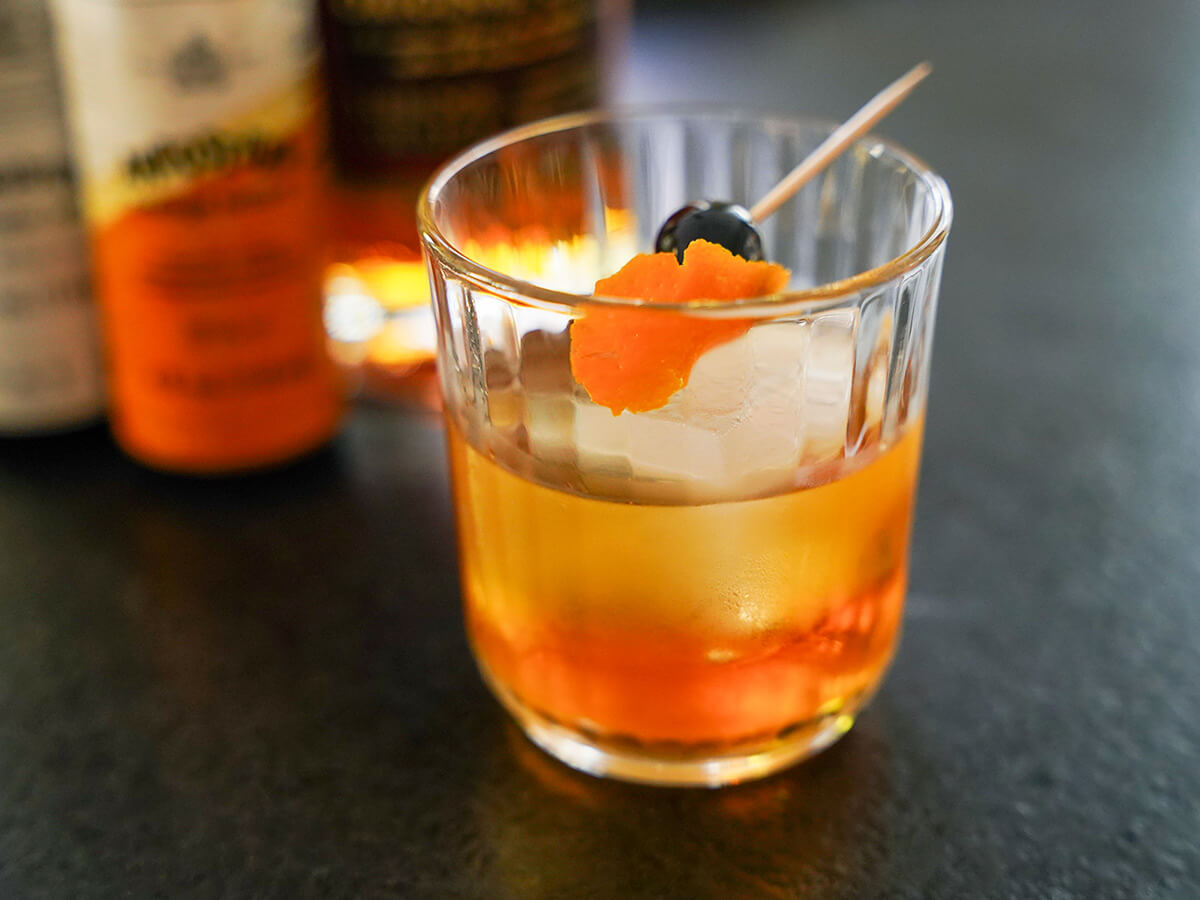 glass of rum old fashioned with light shining in bottles blurred behind.