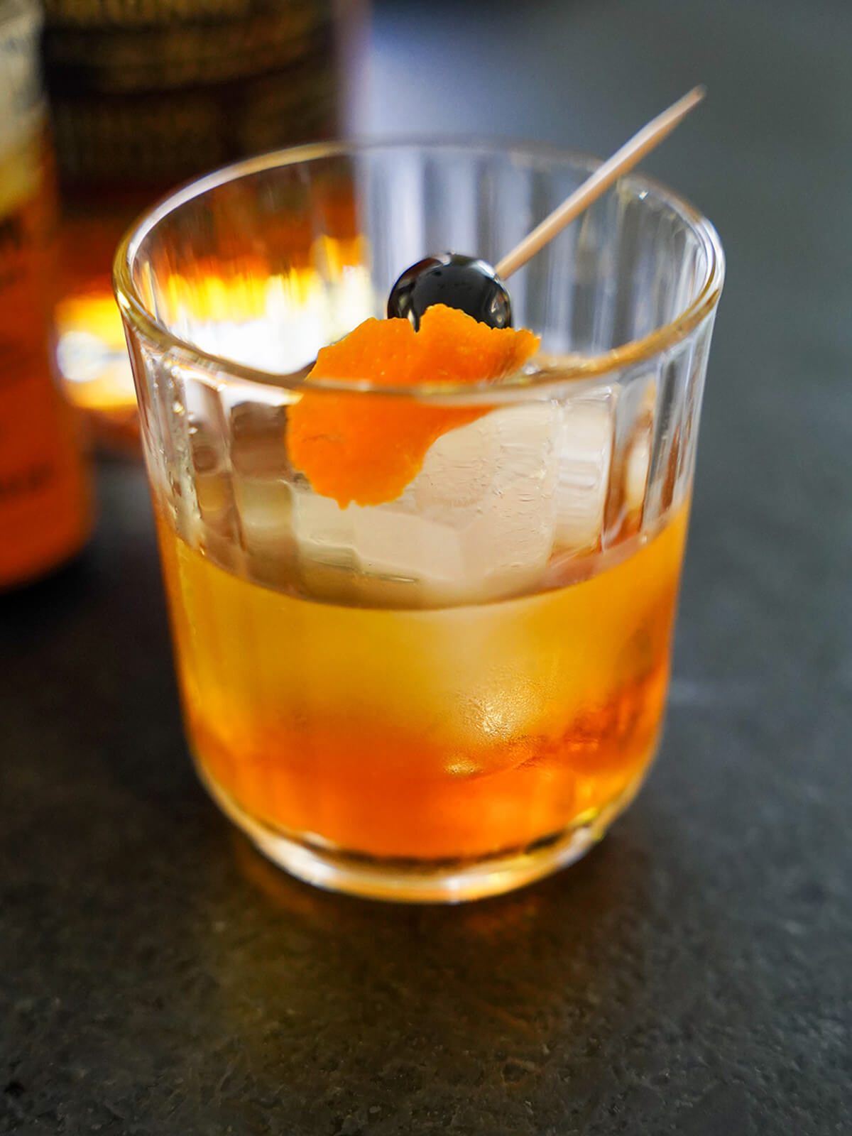 side view of rum old fashioned topped with orange zest and cherry.