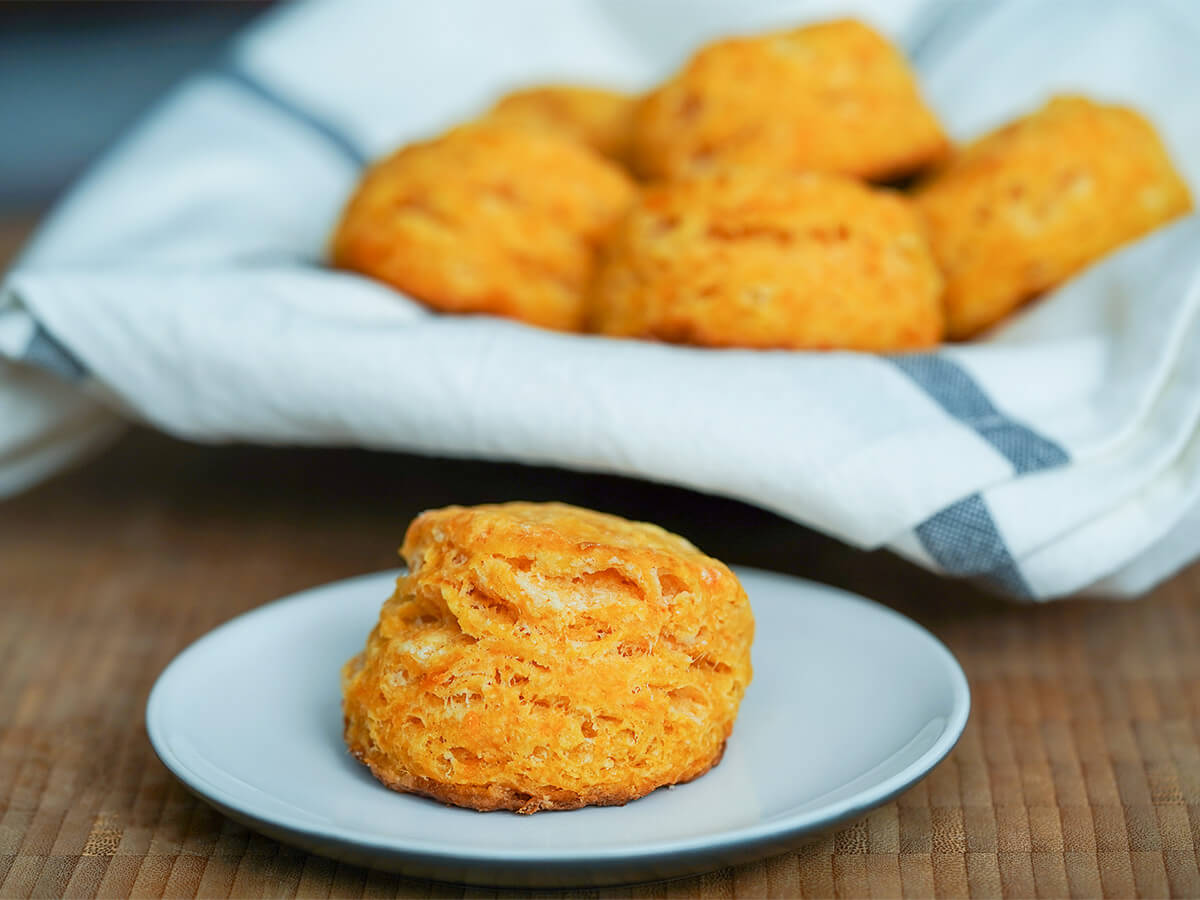 a sweet potato biscuit on plate with more biscuits in cloth in basket behind.