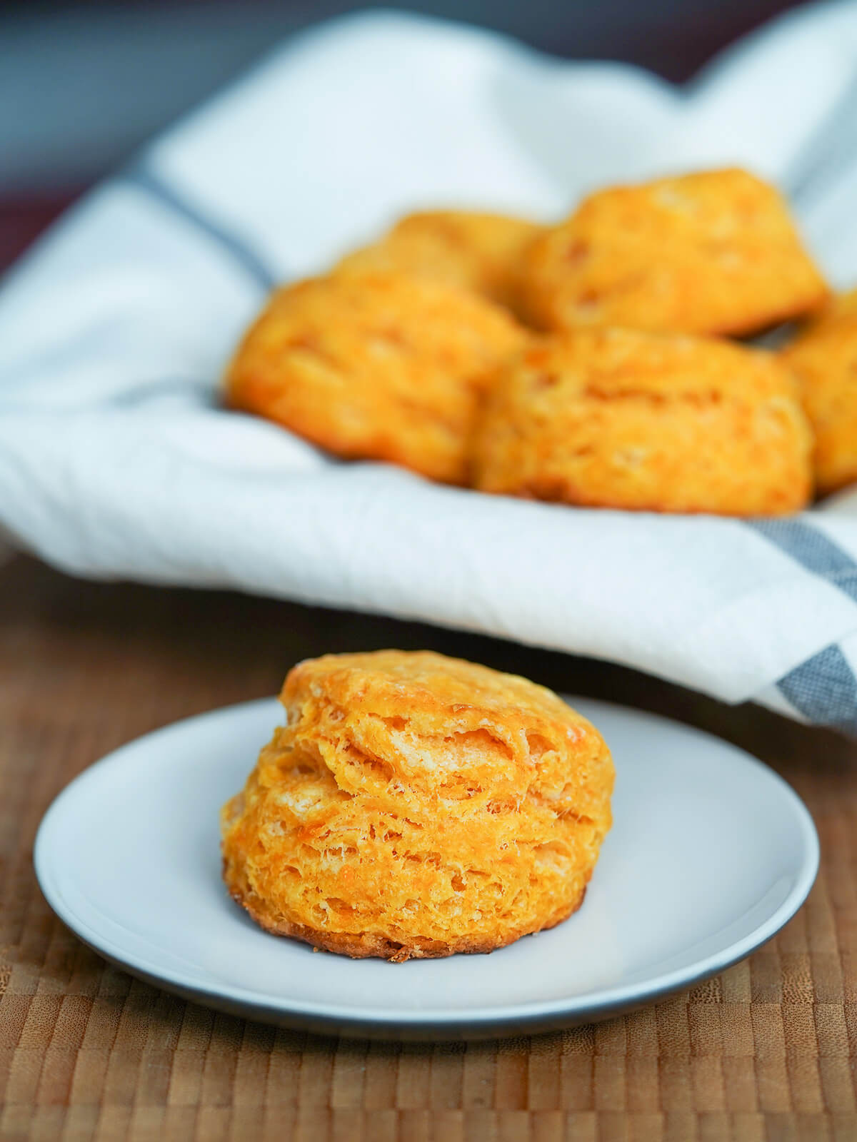 a layered sweet potato biscuit on a plate in front of lined basket with more.