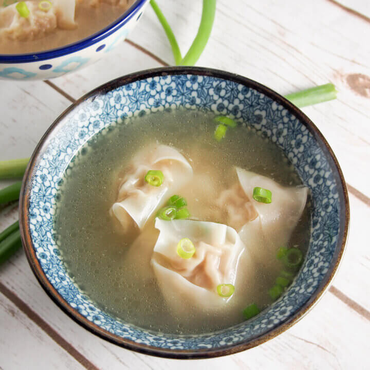 bowl of wonton soup with scallion slices on top of the dumplings at top of soup.