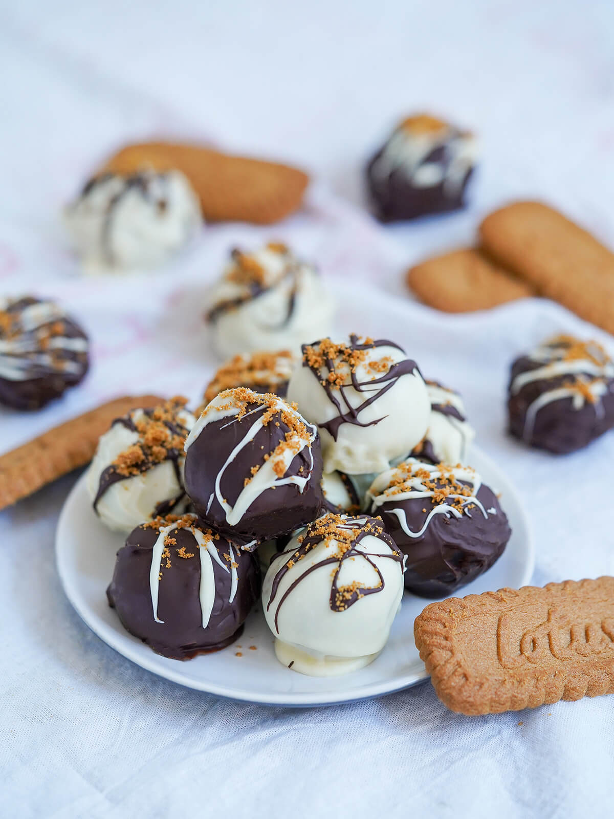 small plate of biscoff truffles with biscoff cookies and additional truffles to side and behind.
