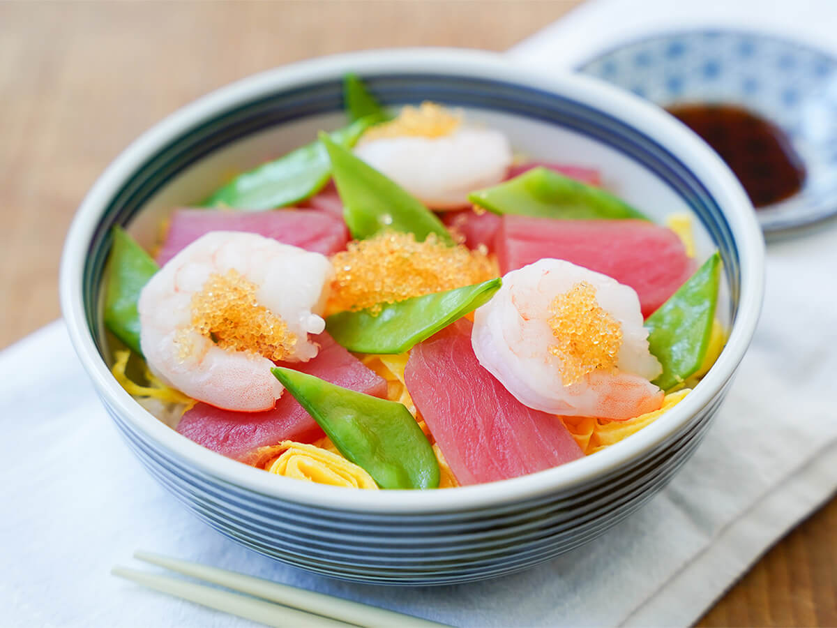bowl of chirashi sushi topped with shrimp, sashimi tuna and cut snow peas.