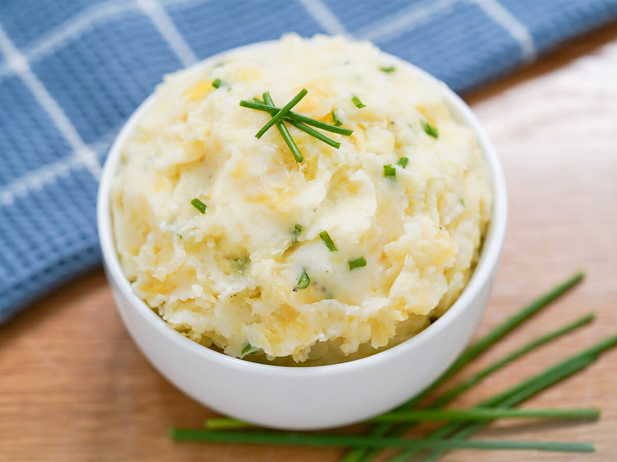 bowl of clapshot potato rutabaga mash with blue cloth behind and chives in front.