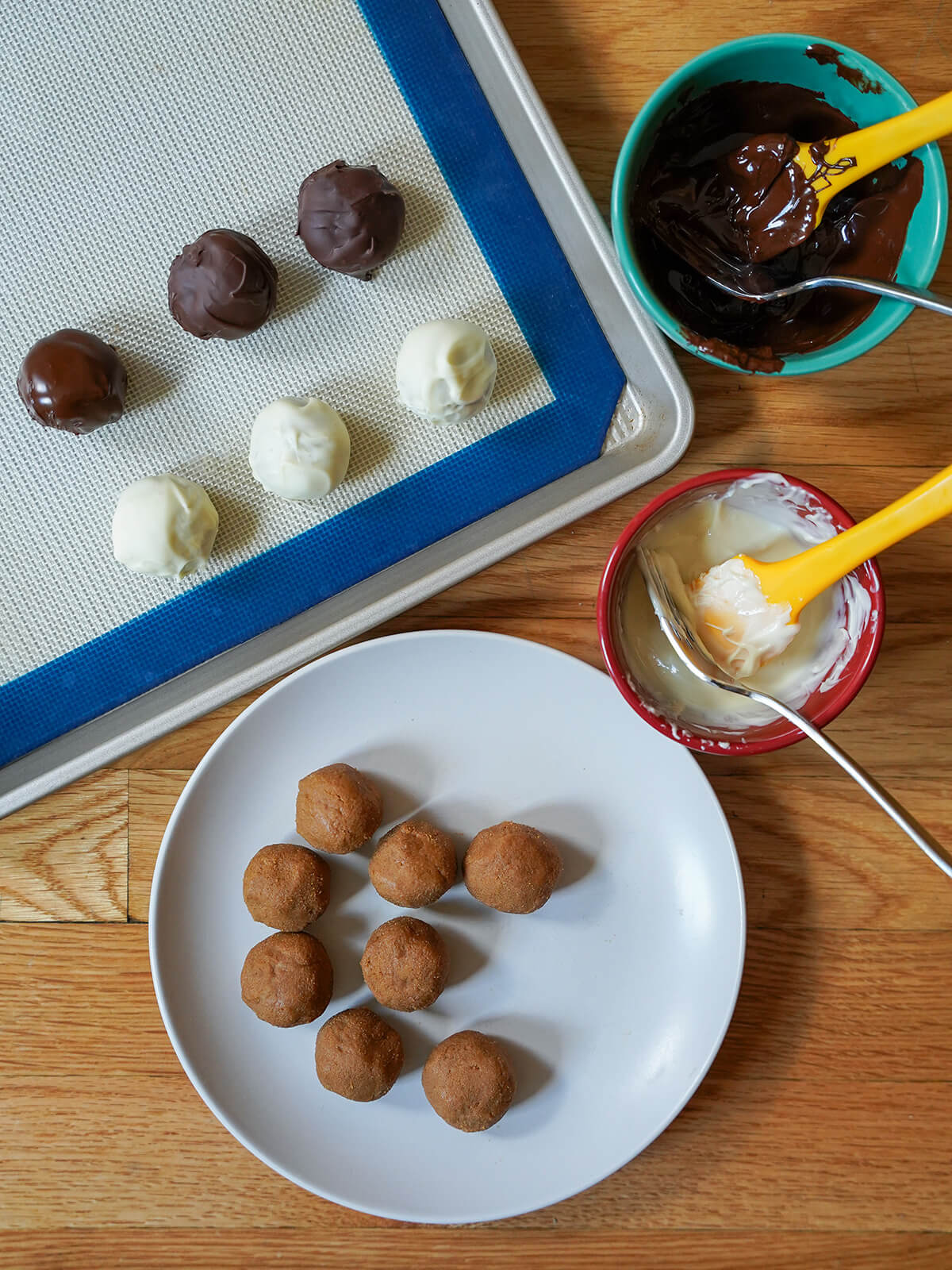 balls of truffle filling on plate with bowls of melted chocolate and some dipped truffles on lined baking sheet.
