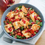 bowl of halloumi pomegranate salad with fork below bowl and cloth under.