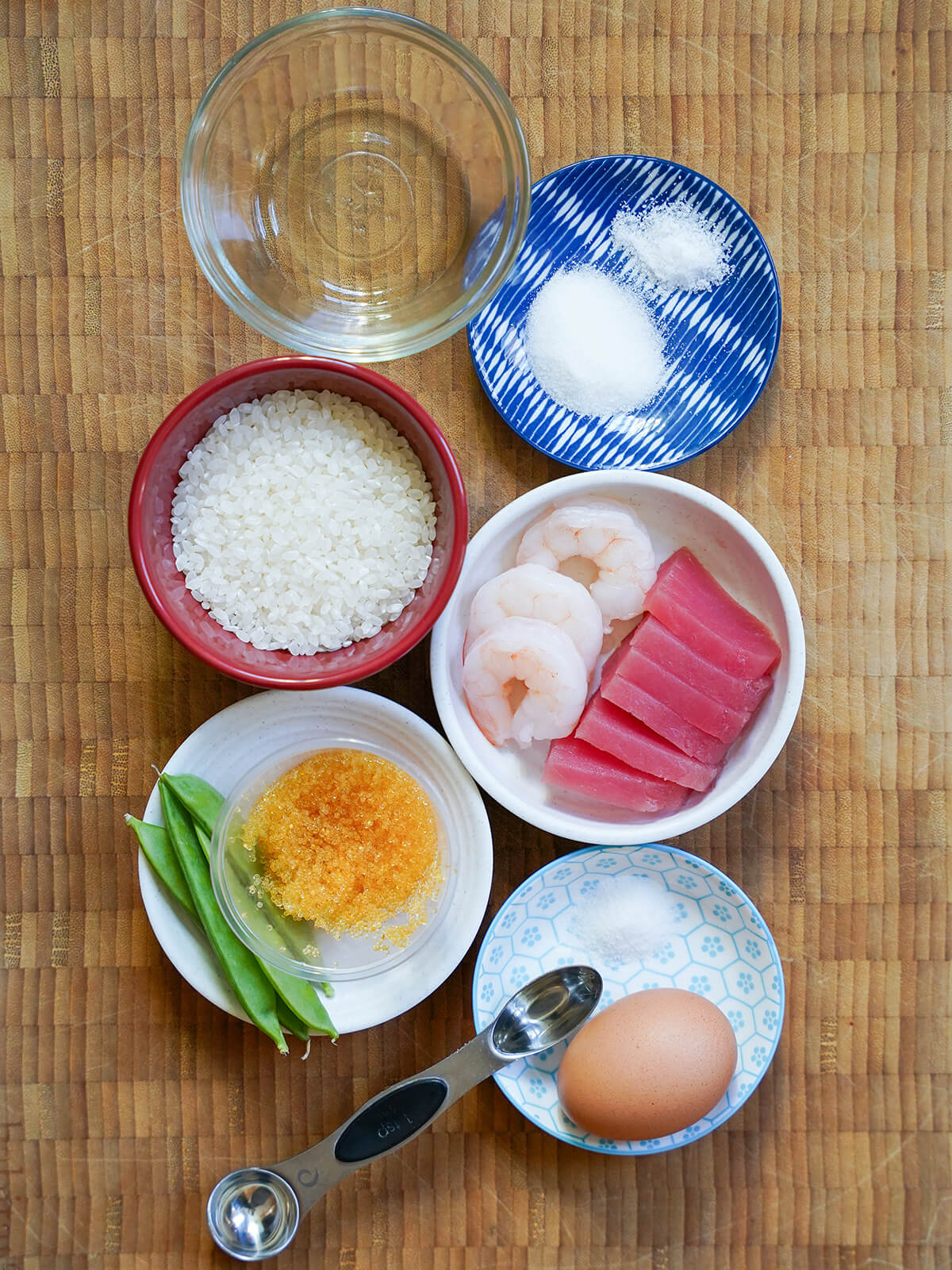 bowls with rice, shrimp, raw tuna slices, egg, fish roe, snow peas, vinegar and other seasonings from overhead.