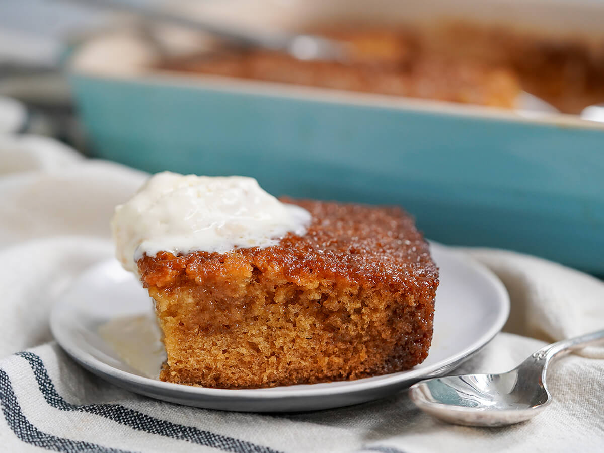slice of malva pudding on plate with spoon to side and dish blurred behind.