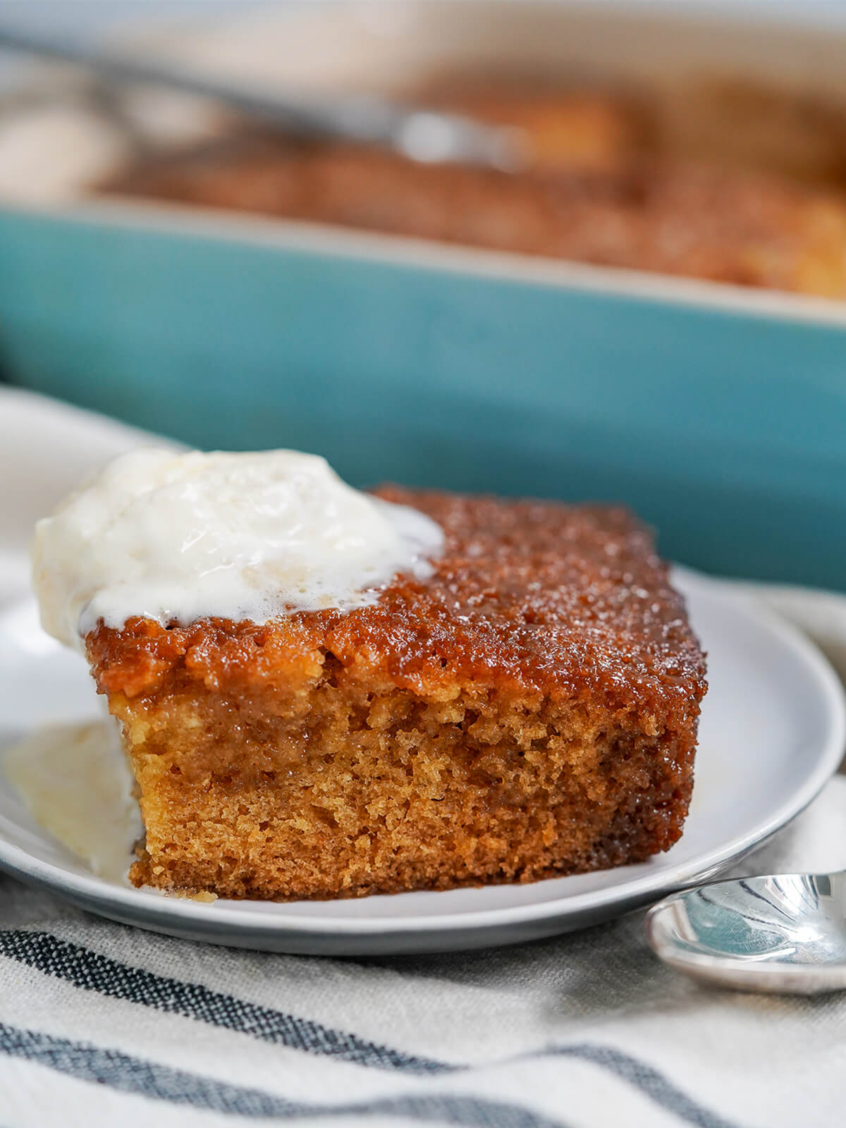 slice of malva pudding on plate topped with melting ice cream and teal dish blurred behind.