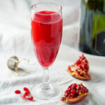 side view of glass of pomegranate mimosa with wedges of pomegranate to side and part botle in background.