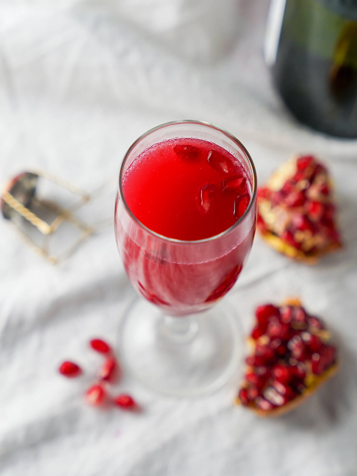This pomegranate mimosa is really easy to make, bright and fruity. It make a great brunch cocktail, perfect for toasting with a festive feel. overhead view of glass of pomegranate mimosa with pomegranate arils floating in drink.