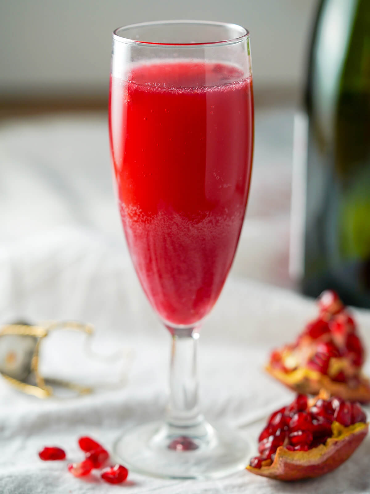 This pomegranate mimosa is really easy to make, bright and fruity. It make a great brunch cocktail, perfect for toasting with a festive feel. side view of a glass of pomegranate mimosa with part of pomegranate below glass.