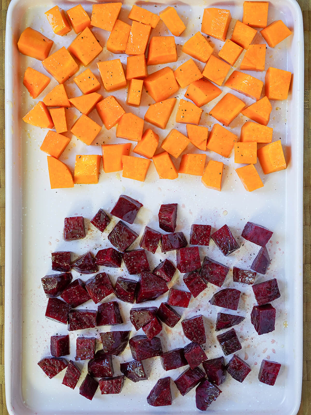cubes of butternut squash at one end and cubes of beet at other end of baking sheet before roasting.