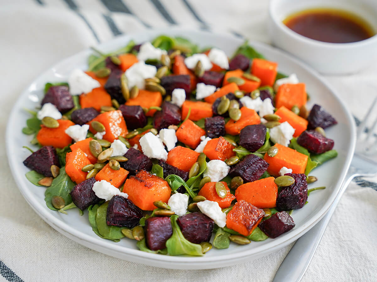 plate of roasted beet and butternut squash salad with dish of dressing sitting behind, slightly blurred.