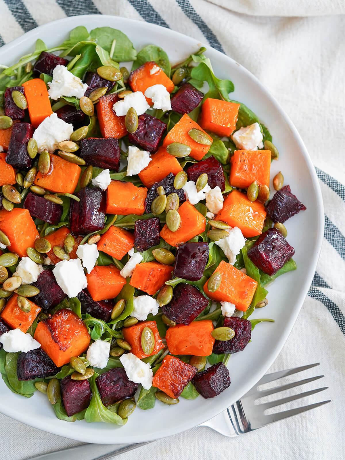 partial overhead view of a plate of roasted beet and butternut squash salad with fork below plate.