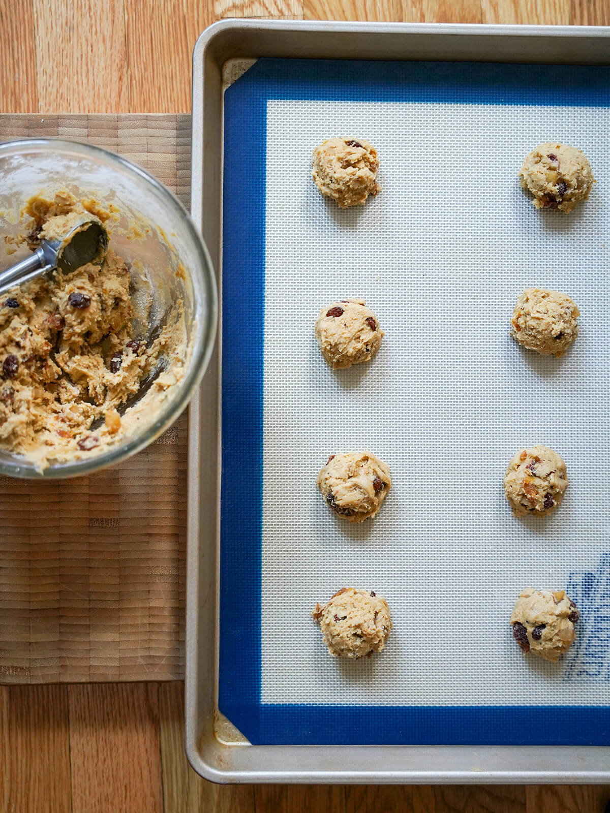 scoops of mincemeat cookie dough on a lined baking sheet with bowl with scoop to side.