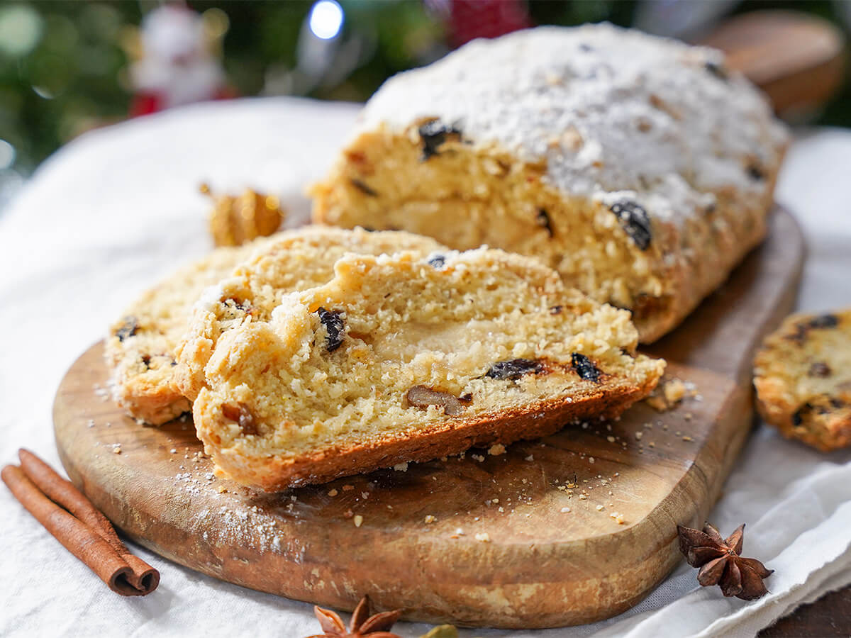 slices in front of rest of whole stollen with prunes on wooden board.