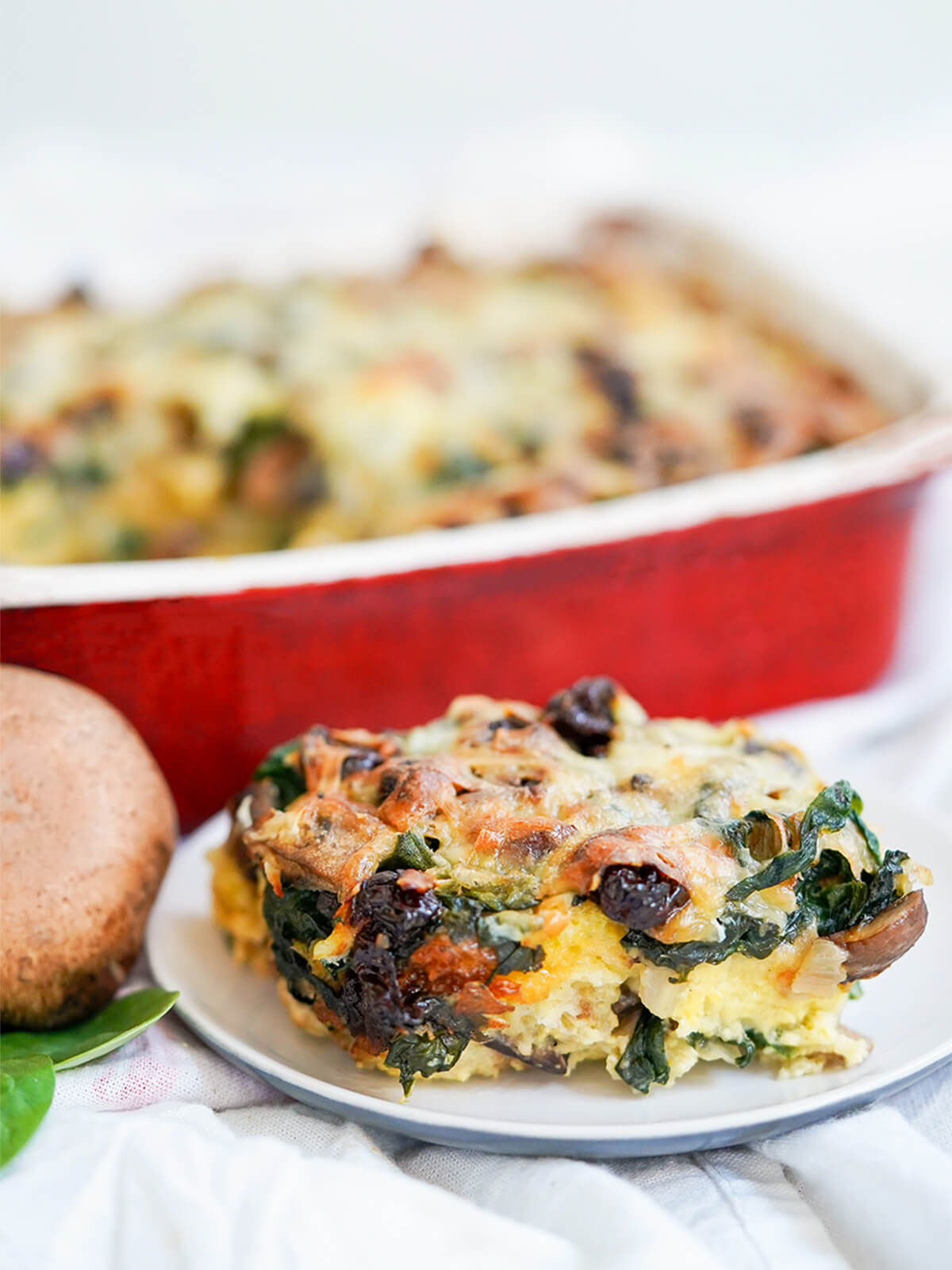 serving of vegetable strata on plate in front of red dish of rest.