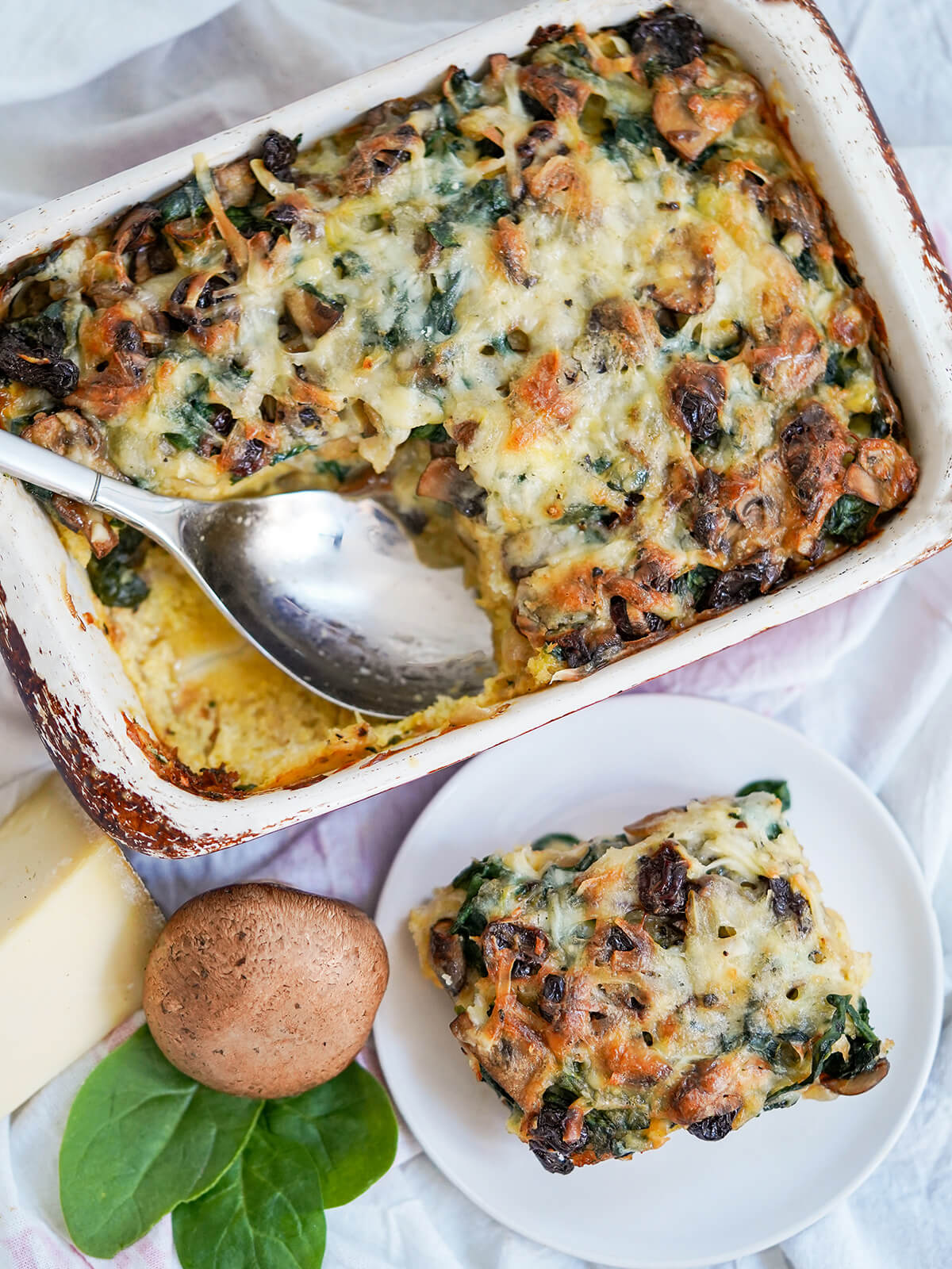 overhead view of some vegetable strata on plate and rest in baking dish with spoon in it.