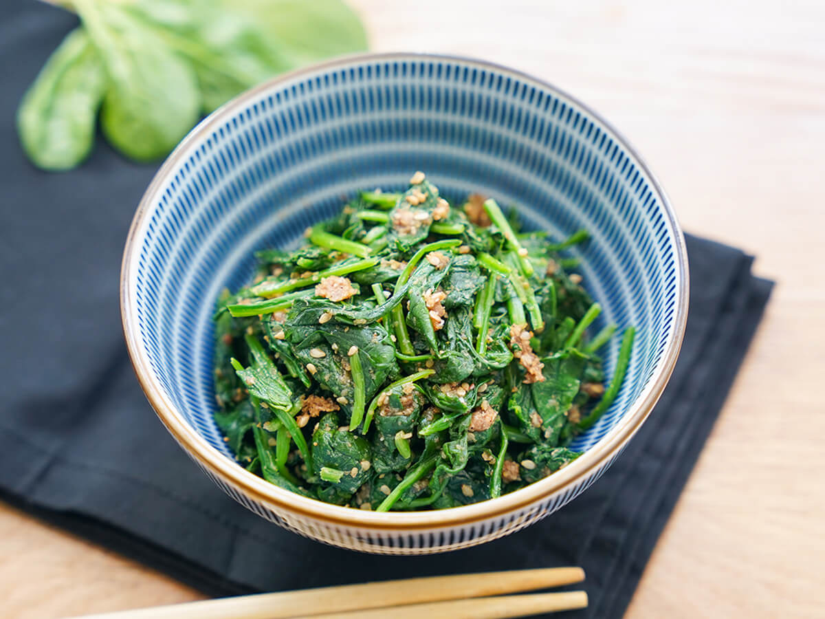 side view of stack of Japanese spinach salad, horenso gomaae, in a blue and white striped bowl.
