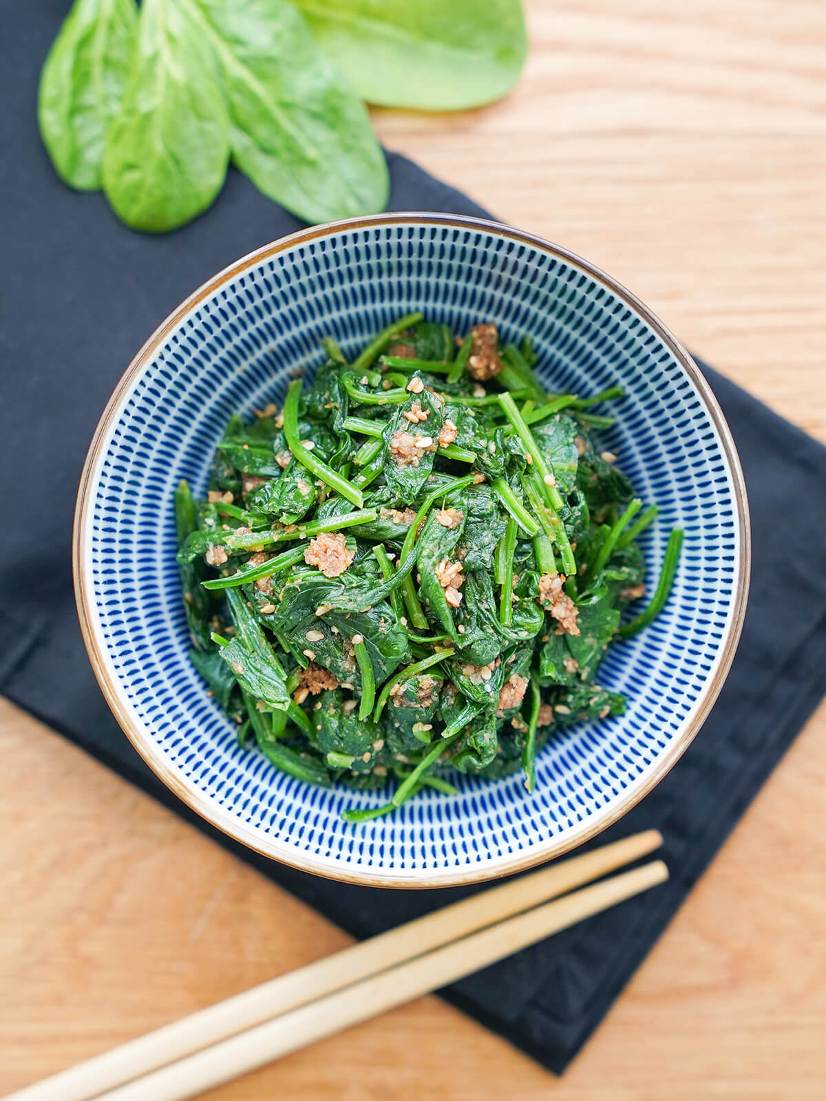 Overhead view of bowl of Japanese spinach salad, spinach gomaae, with chopsticks below bowl.