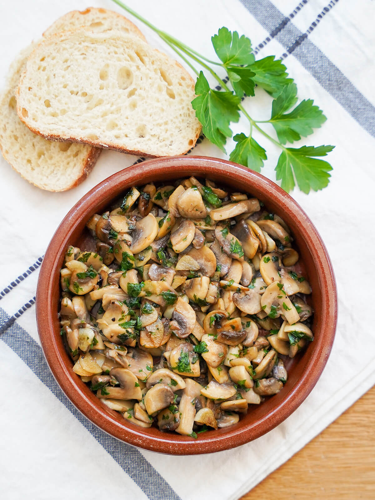 Spanish garlic mushrooms, a classic tapas dish dish of Spanish garlic mushrooms, champiñones al ajillo from overhead with slices of bread and parsley above.