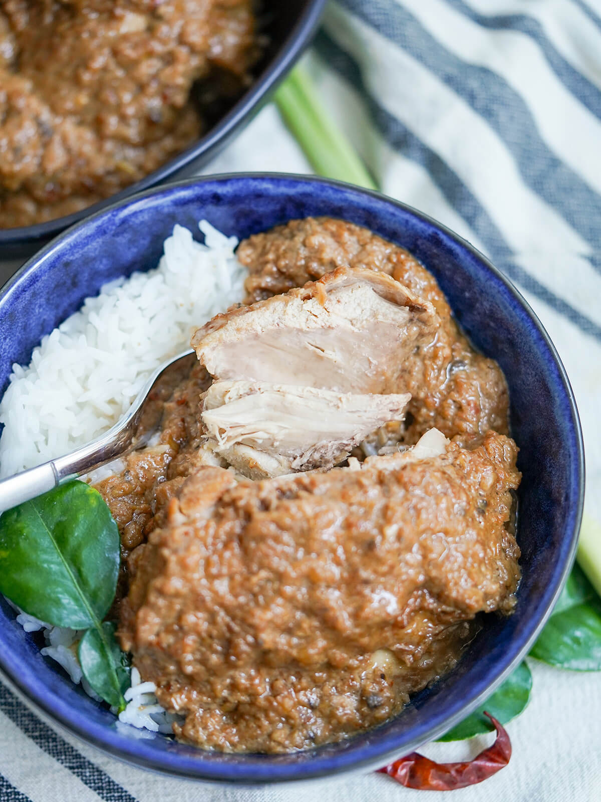 close up view cutting into chicken, fork behind, in bowl of chicken rendang.