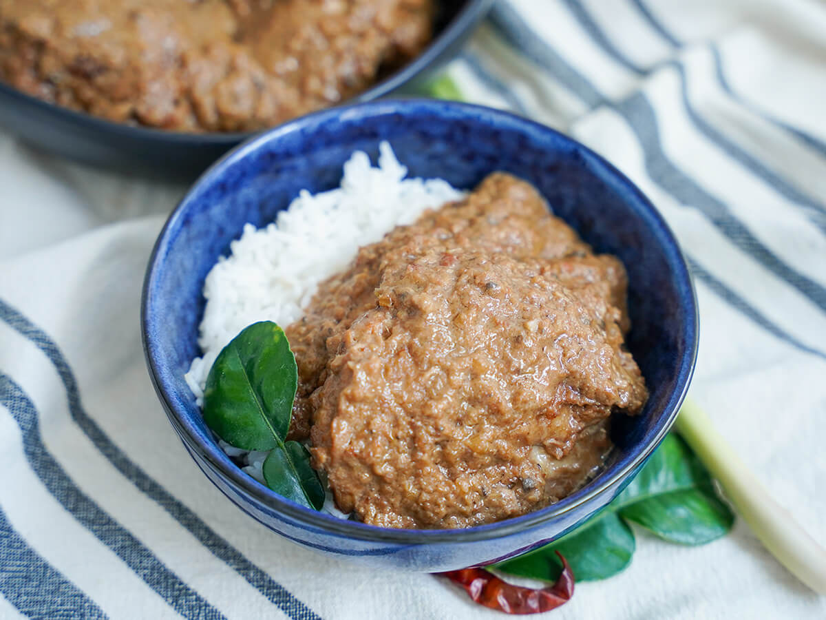 bowl of chicken rendang over rice with lime leaf to side.