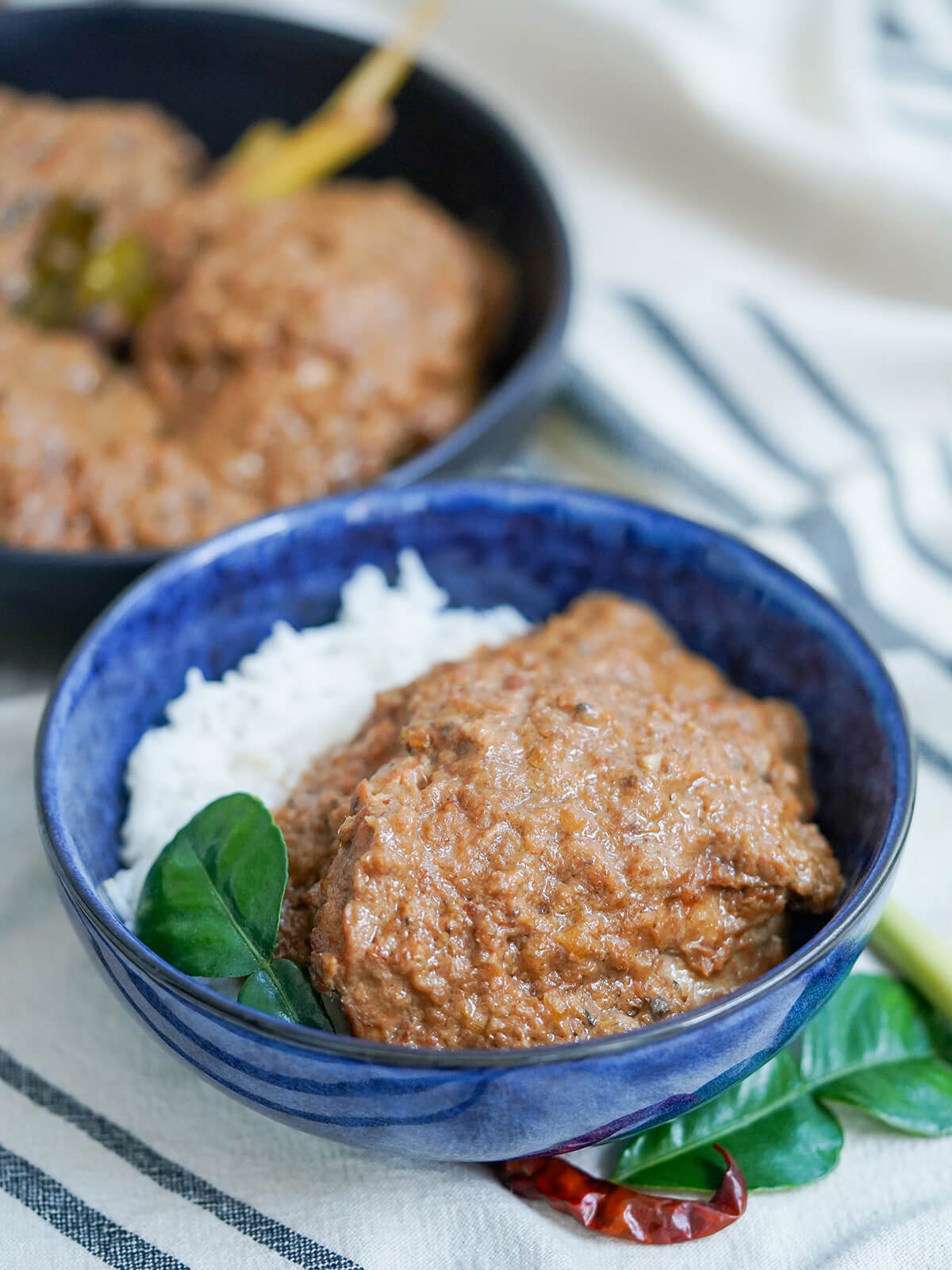 side view of bowl of chicken rendang with pot with more behind.