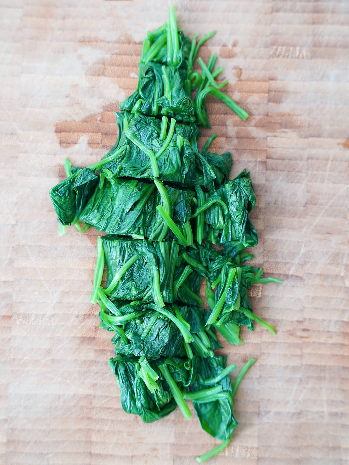 chopped spinach on wooden chopping board.
