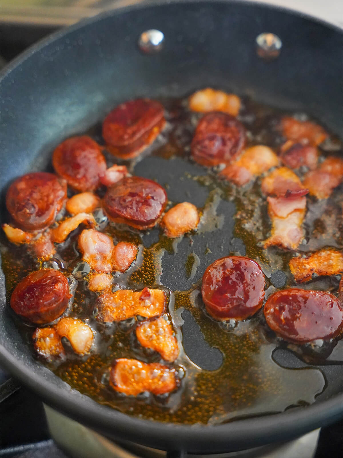 cooking slices of bacon and chorizo in oil in a skillet.
