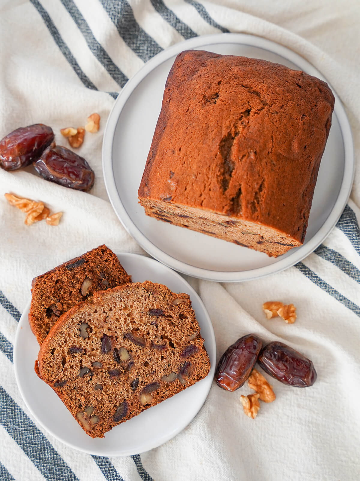 overhead view of part of a date and walnut loaf on one plate with a slice on another and dates and walnut pieces to the side.