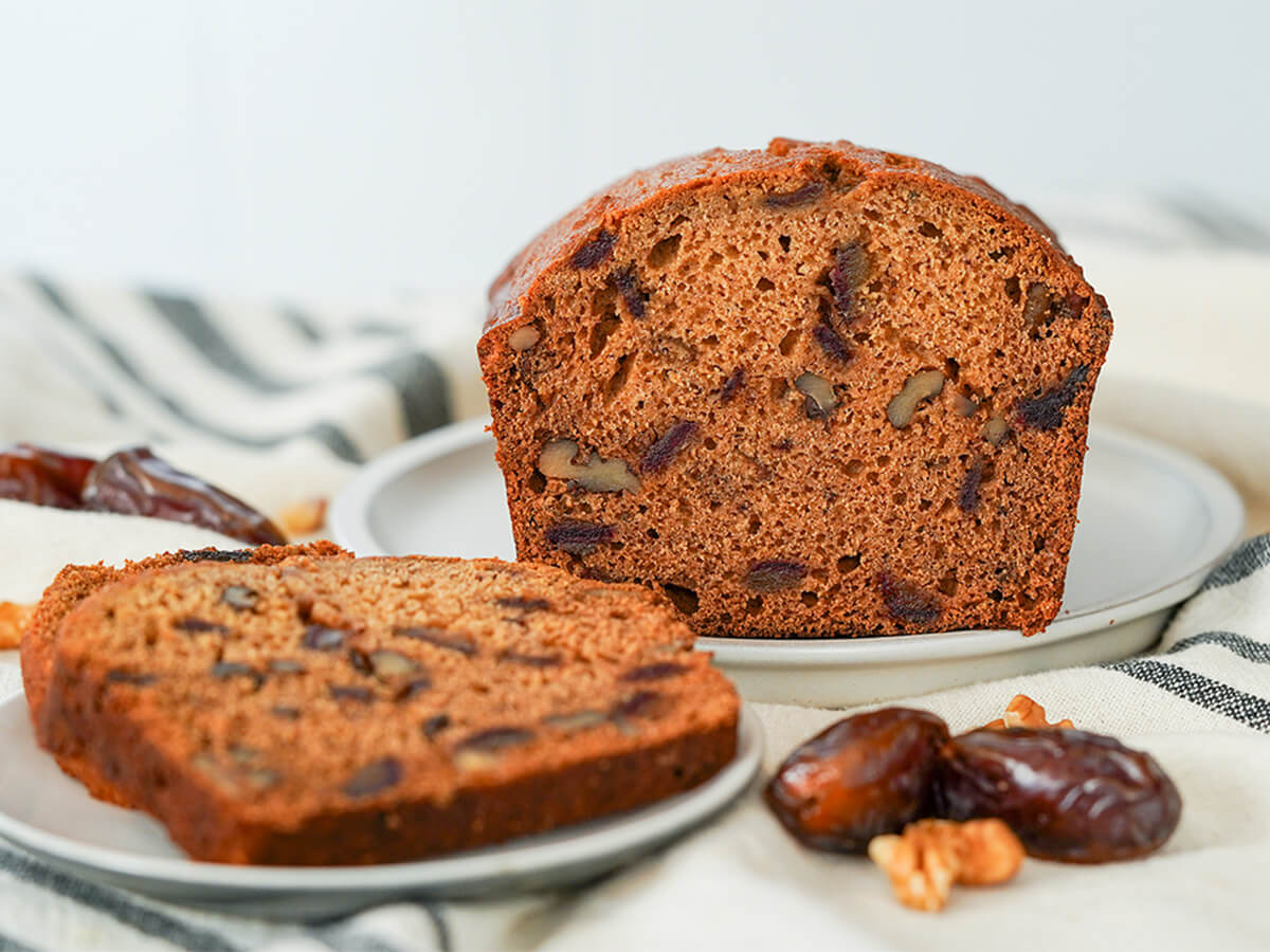 end on view of date and walnut loaf with a slice on a plate in front and dates to side.