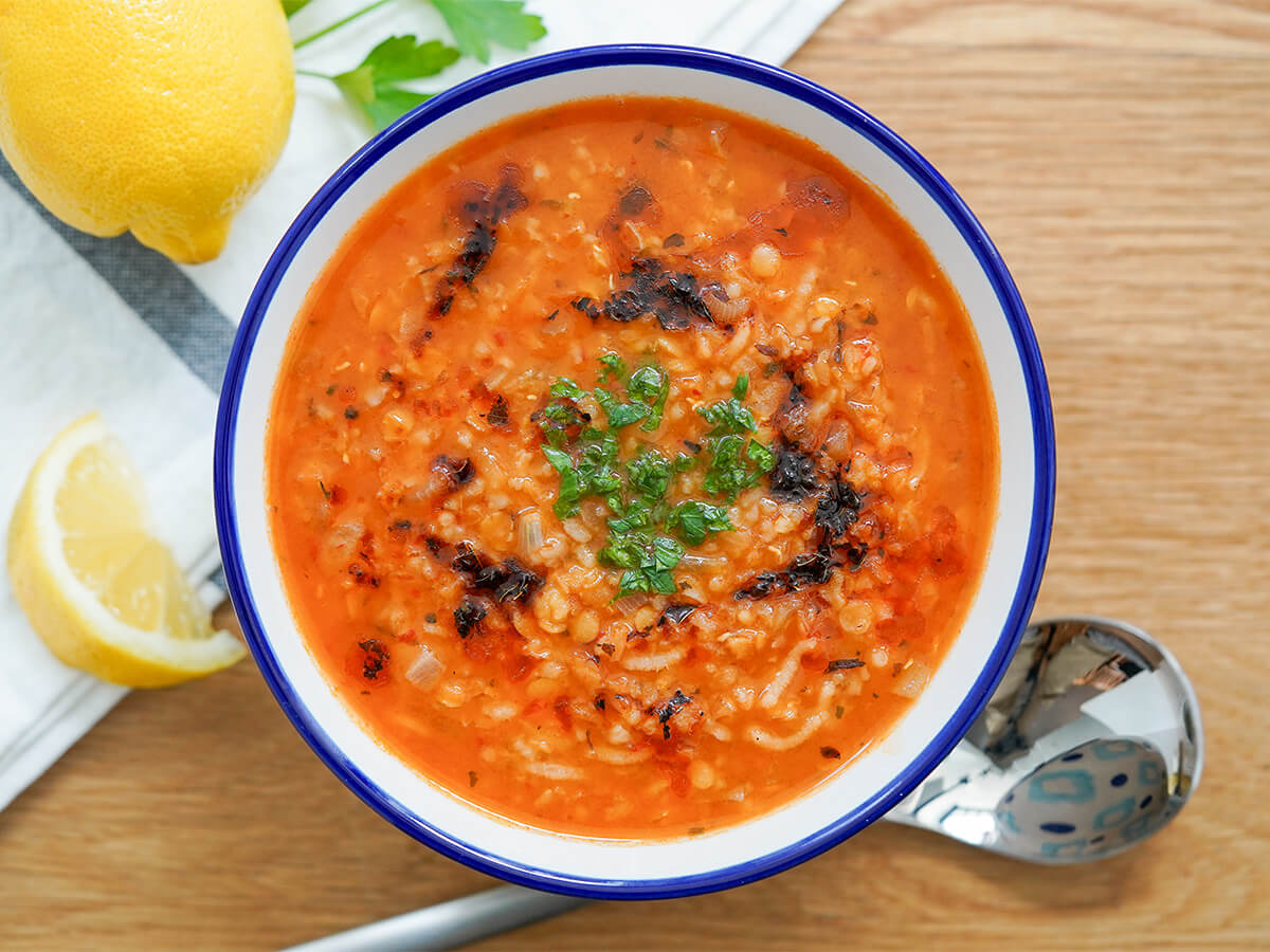 overhead view of bowl of ezogelin soup Turkish lentil bulgur soup with spoon under bowl and lemon to side.