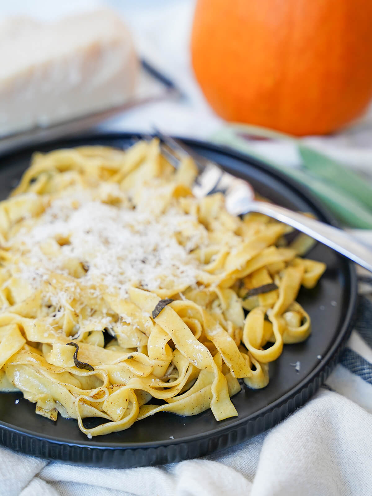 This pumpkin pasta is a delicious way to enjoy a touch of fall in homemade pasta with real pumpkin in the dough. With a subtle savory flavor, and everything that makes homemade pasta so good. side view of plate of fresh pumpkin pasta topped with cheese.