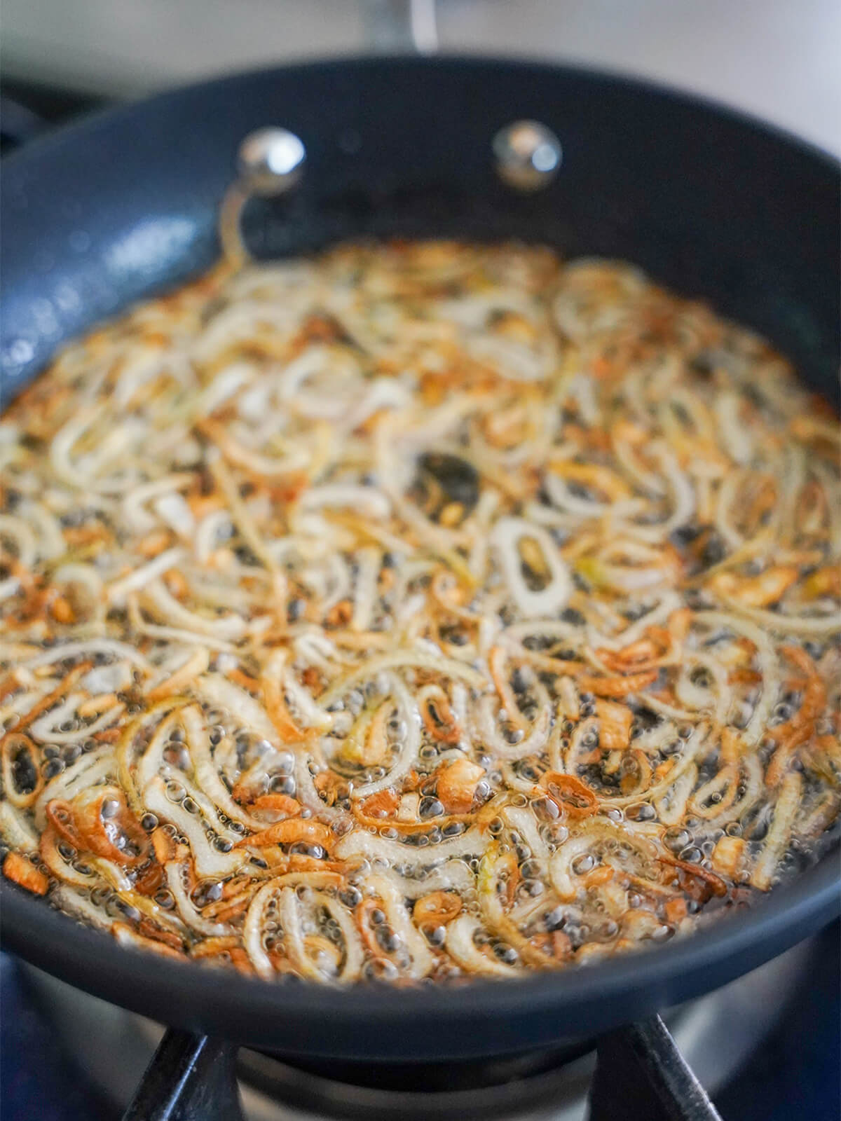 frying sliced shallots in a skillet with oil with some starting to brown.