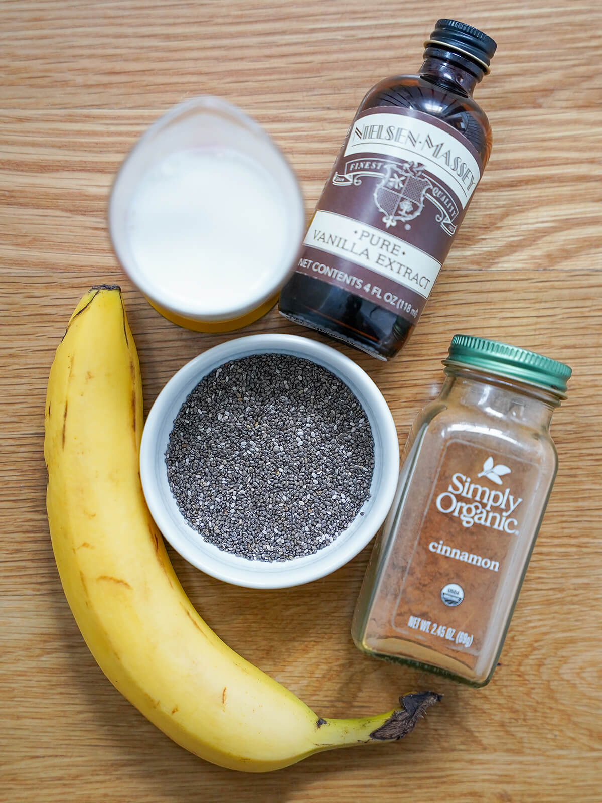 bowl of chia seeds with banana, measure of milk, vanilla and cinnamon around.