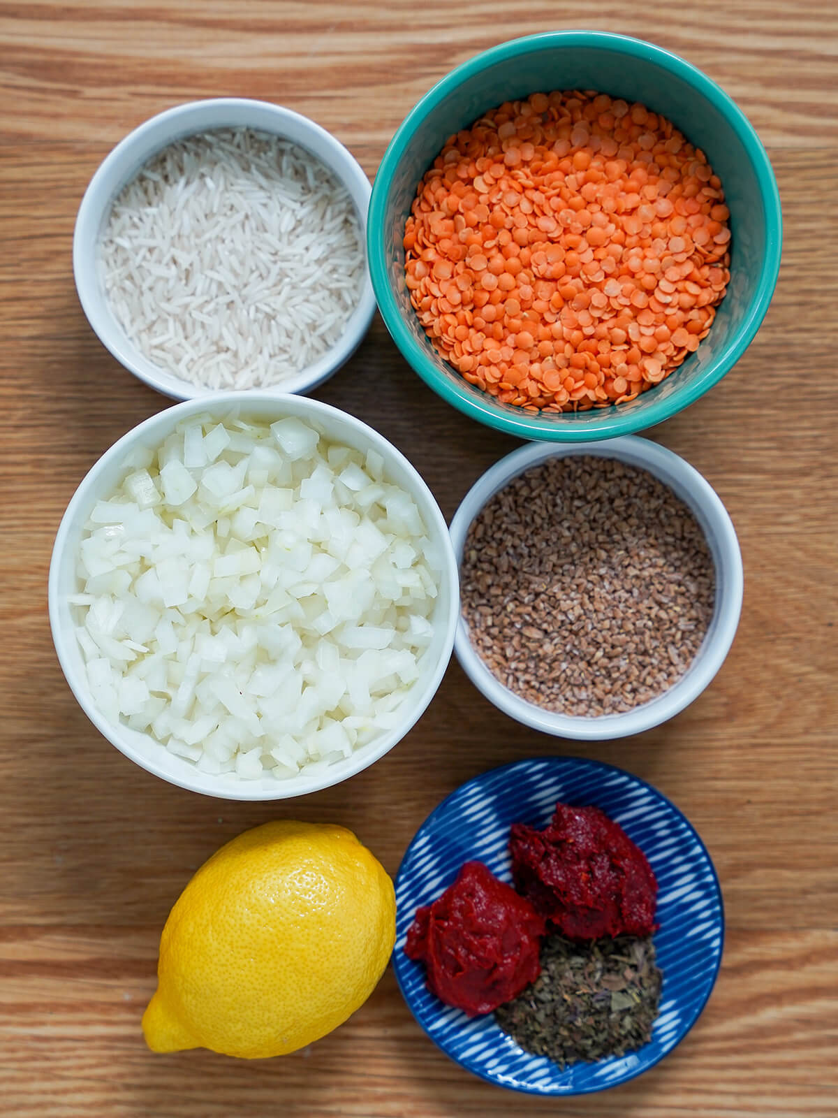 bowls of rice, red lentils, chopped onion, bulgur, and a lemon and dish with tomato and pepper paste and dried mint.