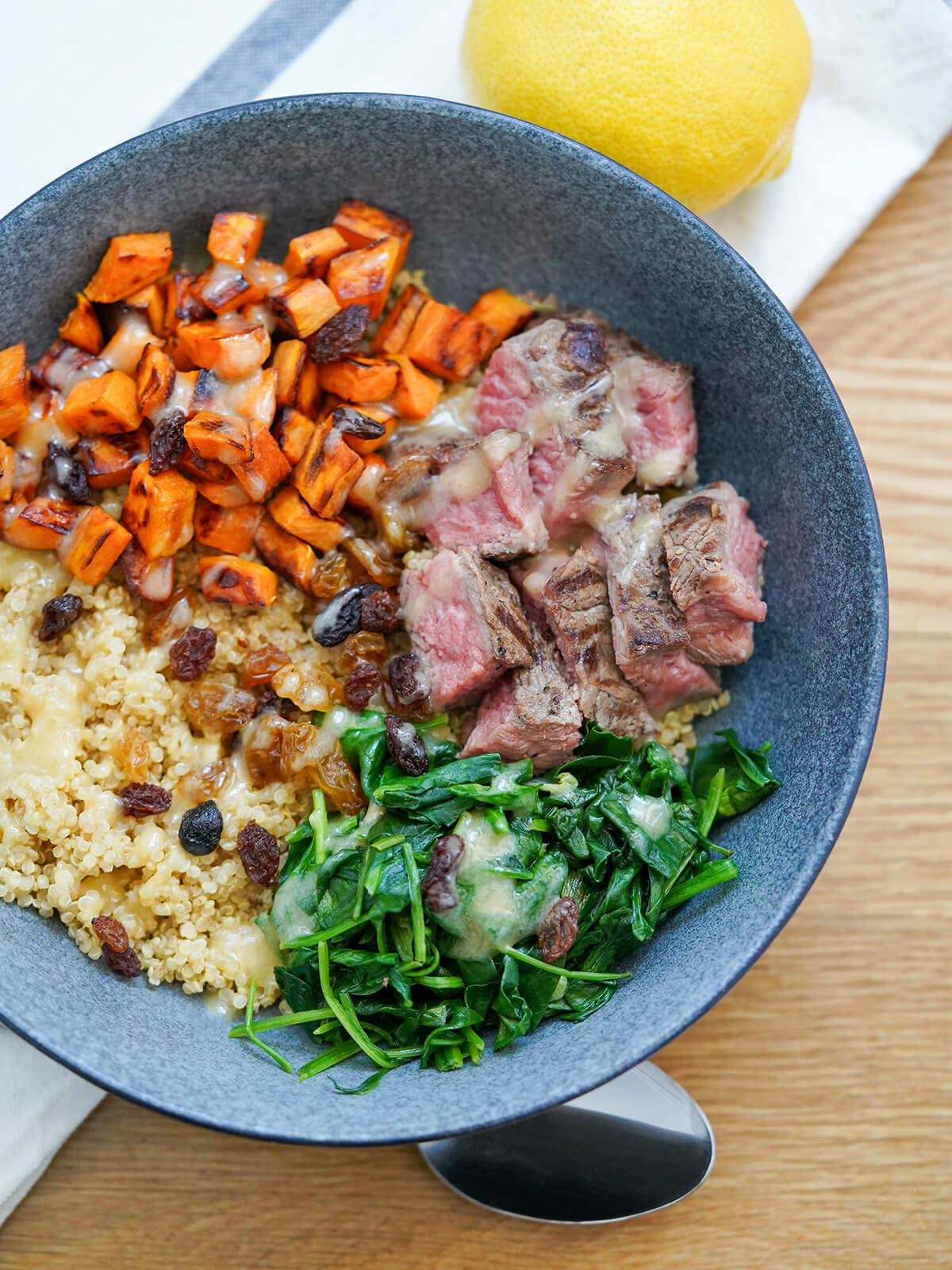 bowl of steak, quinoa, sweet potato and spinach with dressing drizzled over.