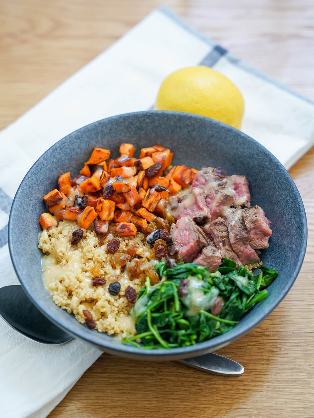 side view of leftover steak and quinoa bowl with lemon behind and spoon below.