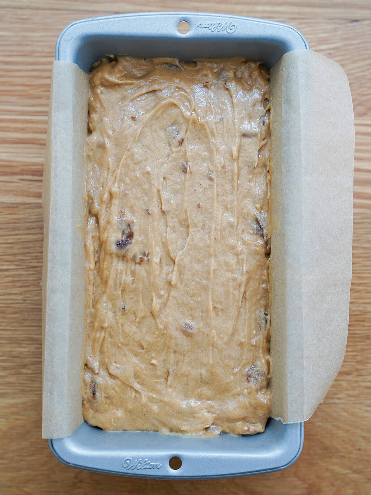 batter in loaf tin with pieces of parchment hanging over sides.