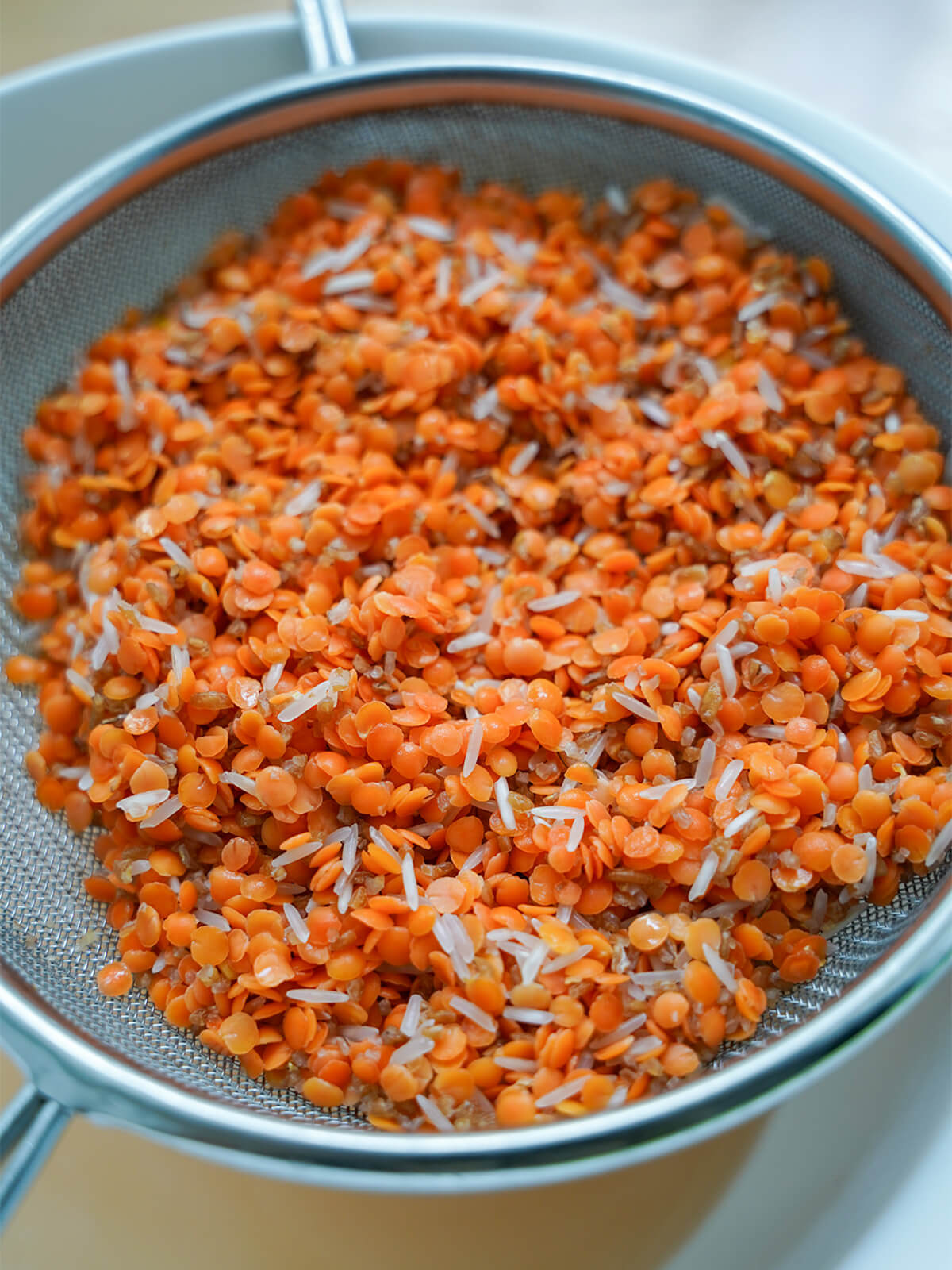 lentils, bulgur and rice in strainer over a bowl after rinsing.