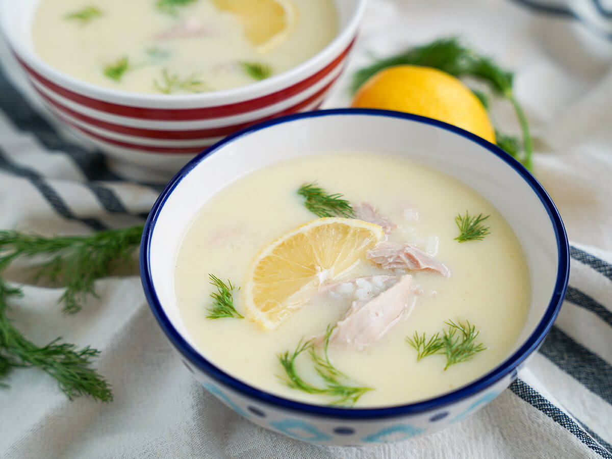 bowl foavgolemono soup with dill to side and part second bowl and lemon behind.